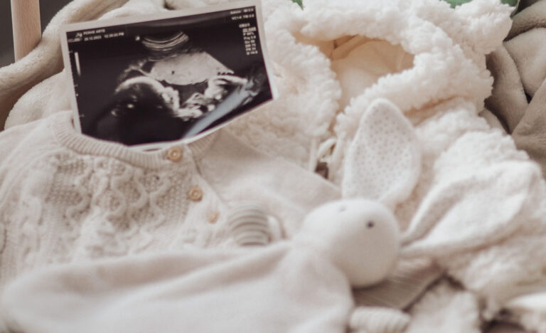 An ultrasound picture, baby clothes and a bunny toy in a crib.